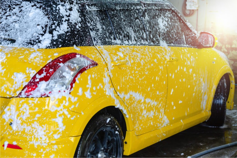 Bright yellow car covered in white soap suds during a professional car wash, highlighting cleanliness and shine.