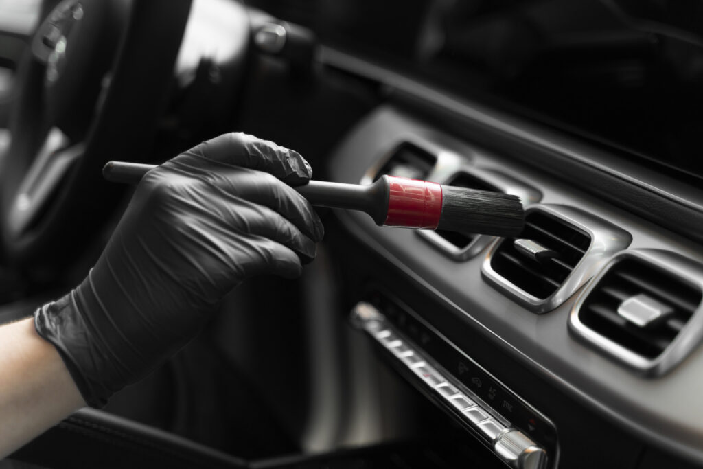Detailer using a brush to clean air vents inside a car, ensuring a pristine interior.